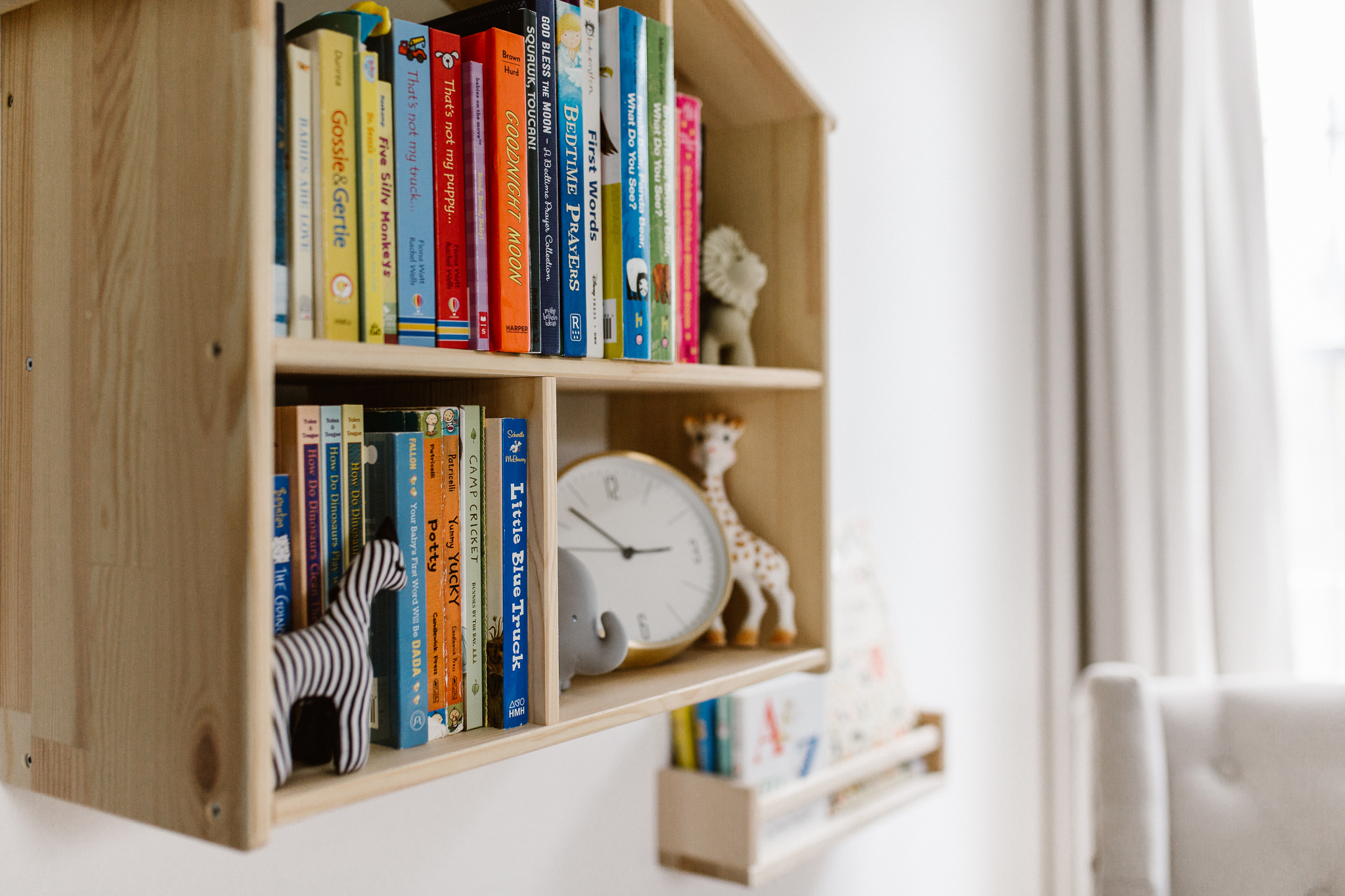 Baby books and toys inside of wooden house shelf on the wall.